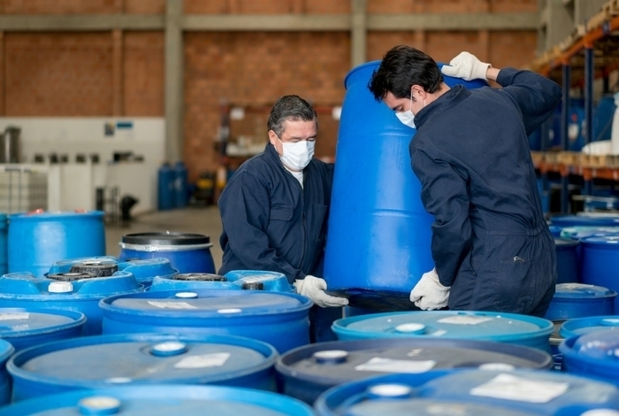 Men working at a chemical plant carrying barrels with toxic products